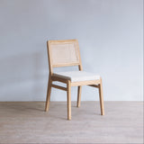 Wooden chair with rattan backrest and white cushion on a plain floor and wall background