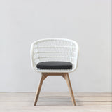 White rattan chair with a black cushion on a light wooden floor and white wall background