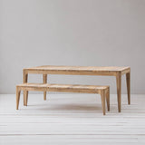 Wooden dining table and bench set on a light wooden floor with a plain background