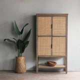 Wooden cabinet with wicker doors and a plant in a woven pot against a gray wall.
