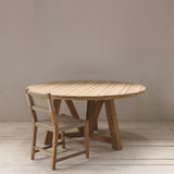 Wooden round dining table with a woven chair on a wooden floor.