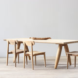 Wooden dining table with three chairs on a light wooden floor against a white wall.