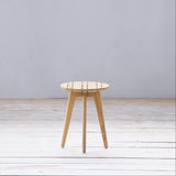 Outdoor round wooden stool with slatted seating on a wooden floor against a plain wall