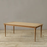 Wooden outdoor dining table on a wooden floor against a plain wall.