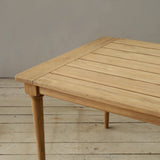Wooden outdoor dining table on a wooden floor against a plain wall.