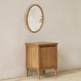 Wooden cabinet against a beige wall with a round mirror above it.