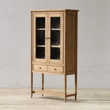 Wooden cabinet with glass doors on a wooden floor against a gray wall