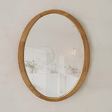 Oval wooden-framed mirror on a white wall
