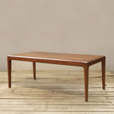 A rectangular wooden dining table with tapered legs and smooth finish, shown on a light wood plank floor against a plain beige wall.