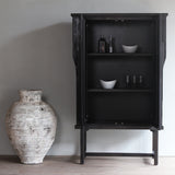 LUNAR Stone Tall Cabinet next to a white vase with both doors opened, showing black interior. Displaying bowls, bottles, and glass inside.