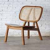 Perspective view of Rattan Lounge Chair. Made from teak wood and rattan webbing. In front of white brick wall.