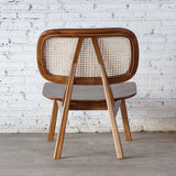 Back view of Rattan Lounge Chair. Made from teak wood and rattan webbing. In front of white brick wall.