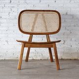 Front view of Rattan Lounge Chair. Made from teak wood and rattan webbing. In front of white brick wall.