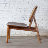 Side view of Rattan Lounge Chair. Made from teak wood and rattan webbing. In front of white brick wall.