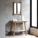 Vanity table with towels and white vase on top of it. There's a mirror hanging above it.