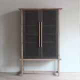 Reclaimed wood tall cabinet with black rattan doors against a plain wall