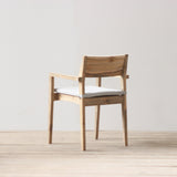 Outdoor wooden armchair with a white cushion on a light wooden floor and gray wall background