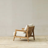 Wooden longue chair with white cushions on a wooden floor against a plain wall