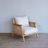 Wooden armchair with white cushions against a grey wall.