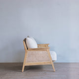 Wooden armchair with white cushions against a light blue wall.
