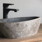 Oval stone sink with black faucet on a wooden surface