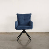 Blue upholstered dining chair on a stone floor against a white wall