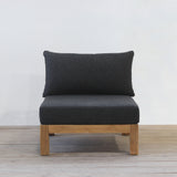 Black cushioned sofa with wooden frame on a light wooden floor and white wall background