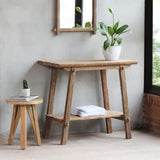 Vanity Table with potted plant on top of it and white towel on the lower shelf. There's small table next to it and a mirror hung on top of it.
