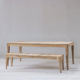 Outdoor dining table and bench set with slatted top against a grey wall.