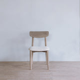 Reclaimed pine wood chair with a beige cushion in a minimalistic room with a light gray wall and wooden floor.