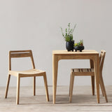 Wooden dining table with two chairs against a plain wall.