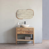 Wooden bathroom vanity with round mirror and sink against a plain wall.