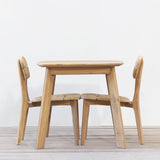 Outdoor wooden square dining table with two chairs set on a wooden floor against a plain wall