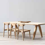 Wooden dining table with three chairs on a light wooden floor against a white wall