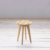 Outdoor round wooden stool with slatted seating on a wooden floor against a plain wall