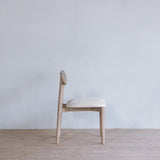 Reclaimed pine wood chair with a beige cushion on a wooden floor against a light gray wall.