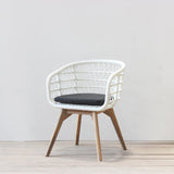 White rattan chair with wooden legs and a black cushion on a light wooden floor.