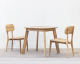 Outdoor wooden square dining table with two chairs set on a wooden floor against a plain wall
