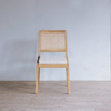 Wooden chair with rattan backrest against a plain wall.