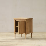 Wooden bathroom cabinet with one door open on a wooden floor and beige wall background