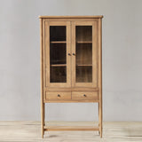 Wooden cabinet with glass doors on a wooden floor against a gray wall