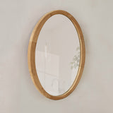 Oval wooden-framed mirror on a plain wall