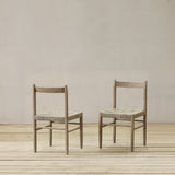 Two wooden chairs with woven seats on a wooden floor against a plain wall.