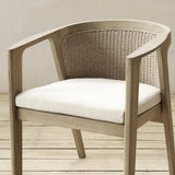 A modern armchair with a beige wood frame, a woven backrest, and a white cushioned seat, set against a neutral beige wall and light wood floor.