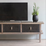 Wooden TV cabinet with a television and plant against a light wall.