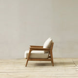 Wooden longue chair with white cushions on a wooden floor against a plain wall