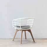 White rattan chair with wooden legs on a light wooden floor and white wall background