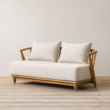Outdoor sofa with wooden frame and white cushions against a plain wall.