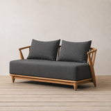 Outdoor sofa with wooden frame and black cushions against a plain wall.