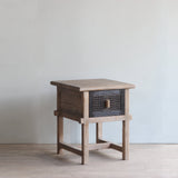 Wooden side table with rattan drawer on a light wooden floor.